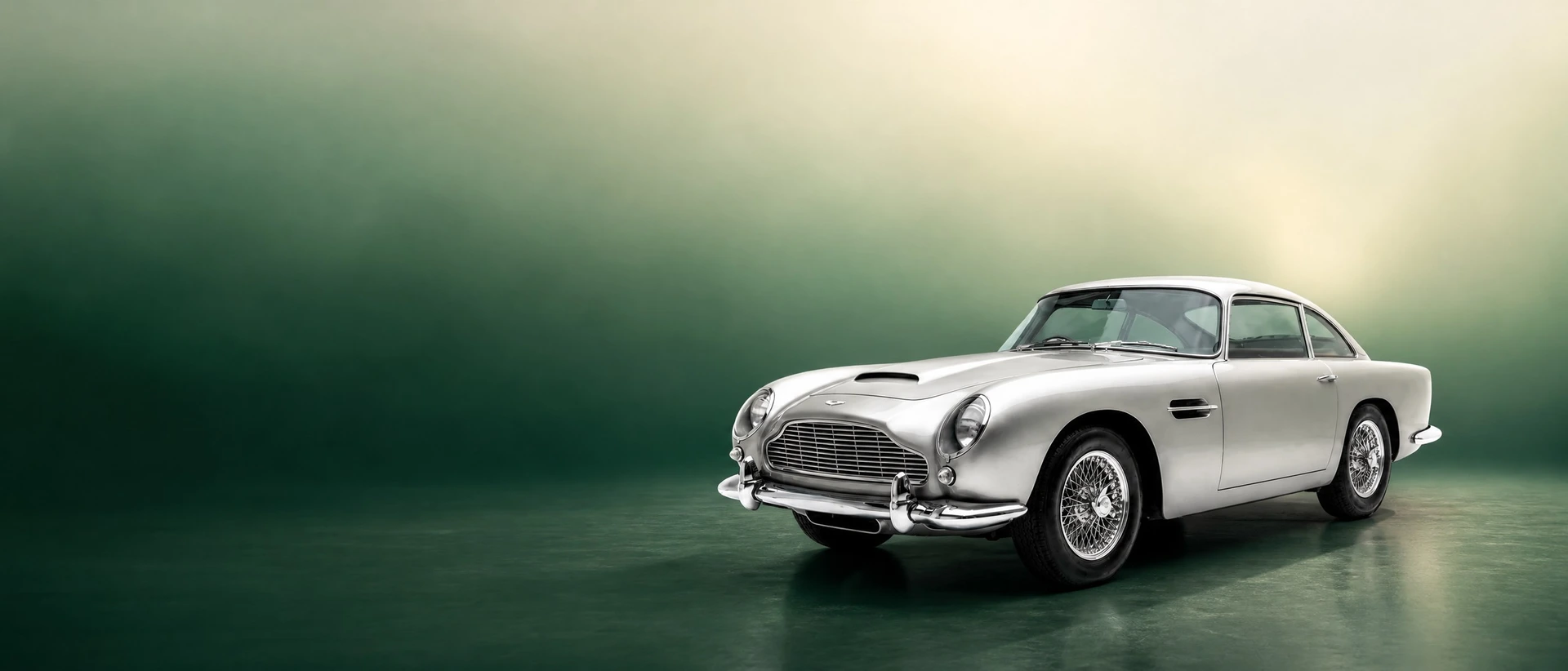 An Aston Martin DB4, front three-quarter view on a racing-green gradient field