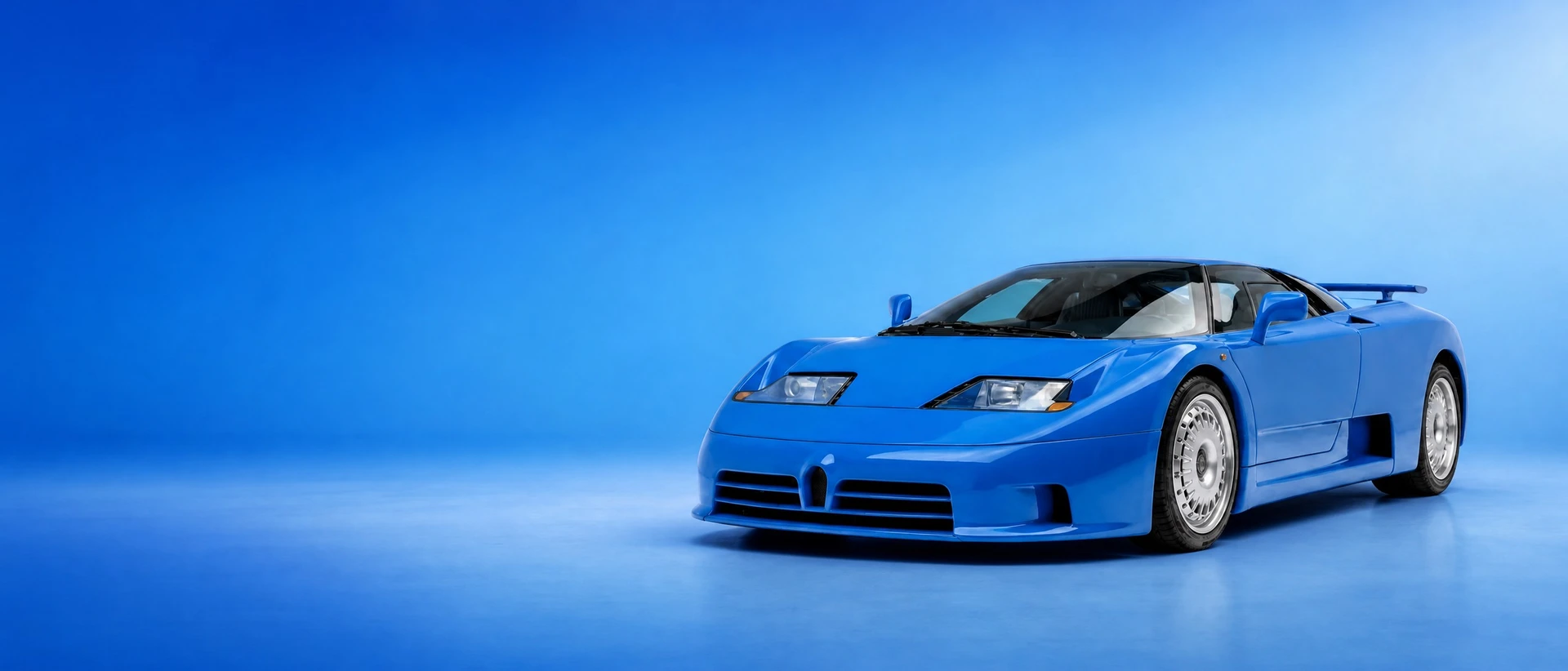 A blue Bugatti EB110, front three-quarter view on a French-blue gradient field