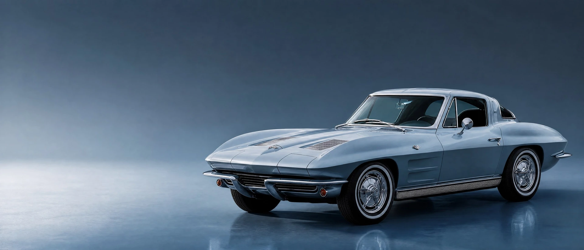 A Silver Blue 1963 Corvette Sting Ray split-window coupé, front three-quarter view on a deep steel-blue field in cool daylight