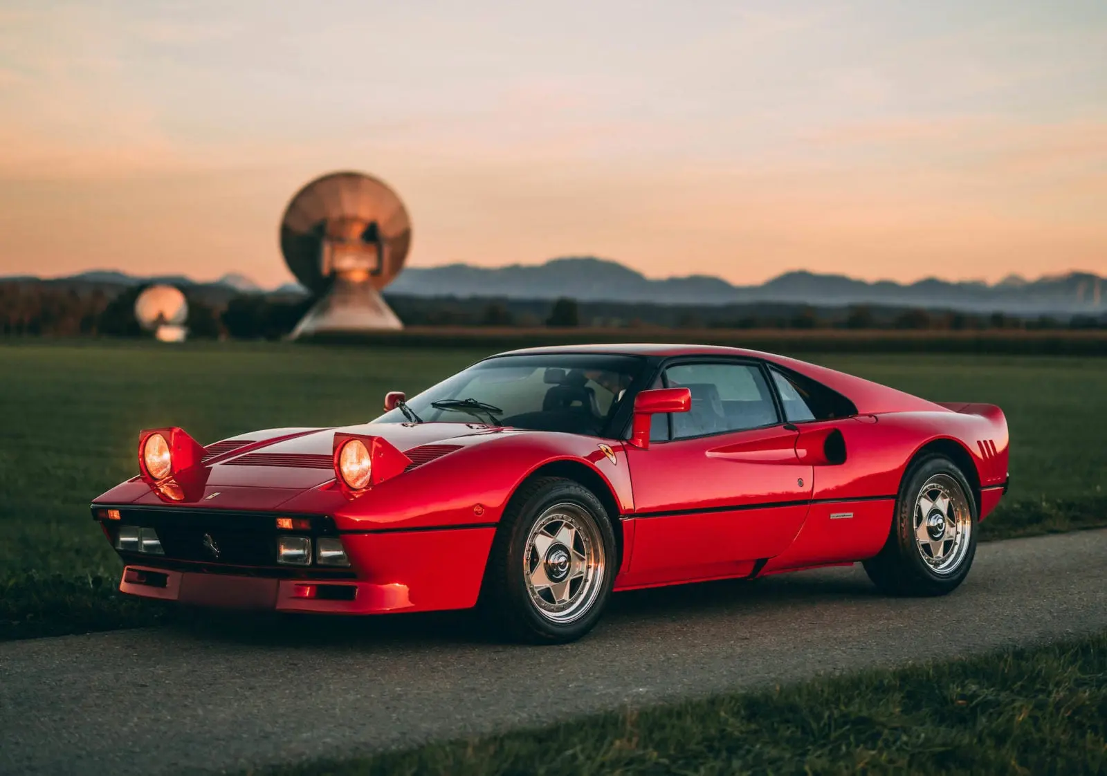 Red Ferrari 288 GTO with raised pop-up headlights in front-three-quarter view at an outdoor radome facility.