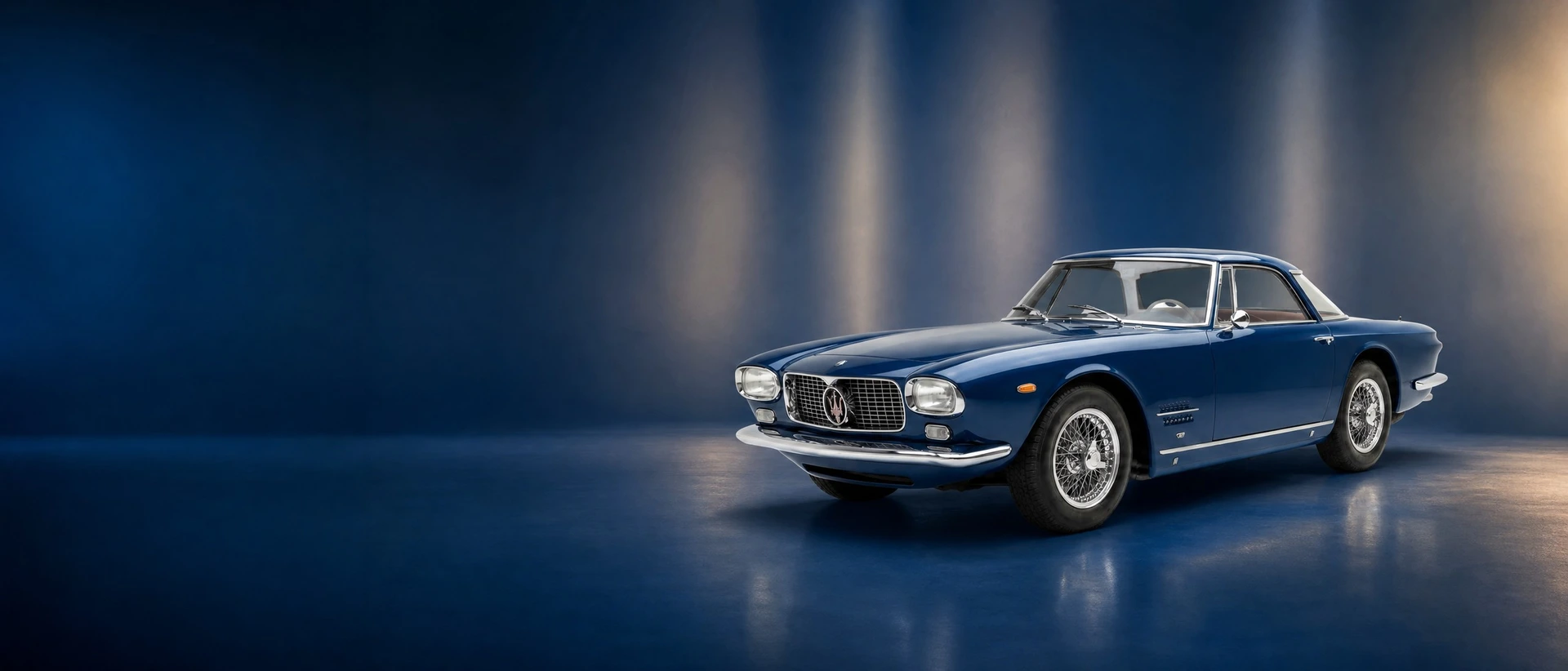 A blue Maserati 5000 GT, front three-quarter view on a deep-blue field with tall light bands