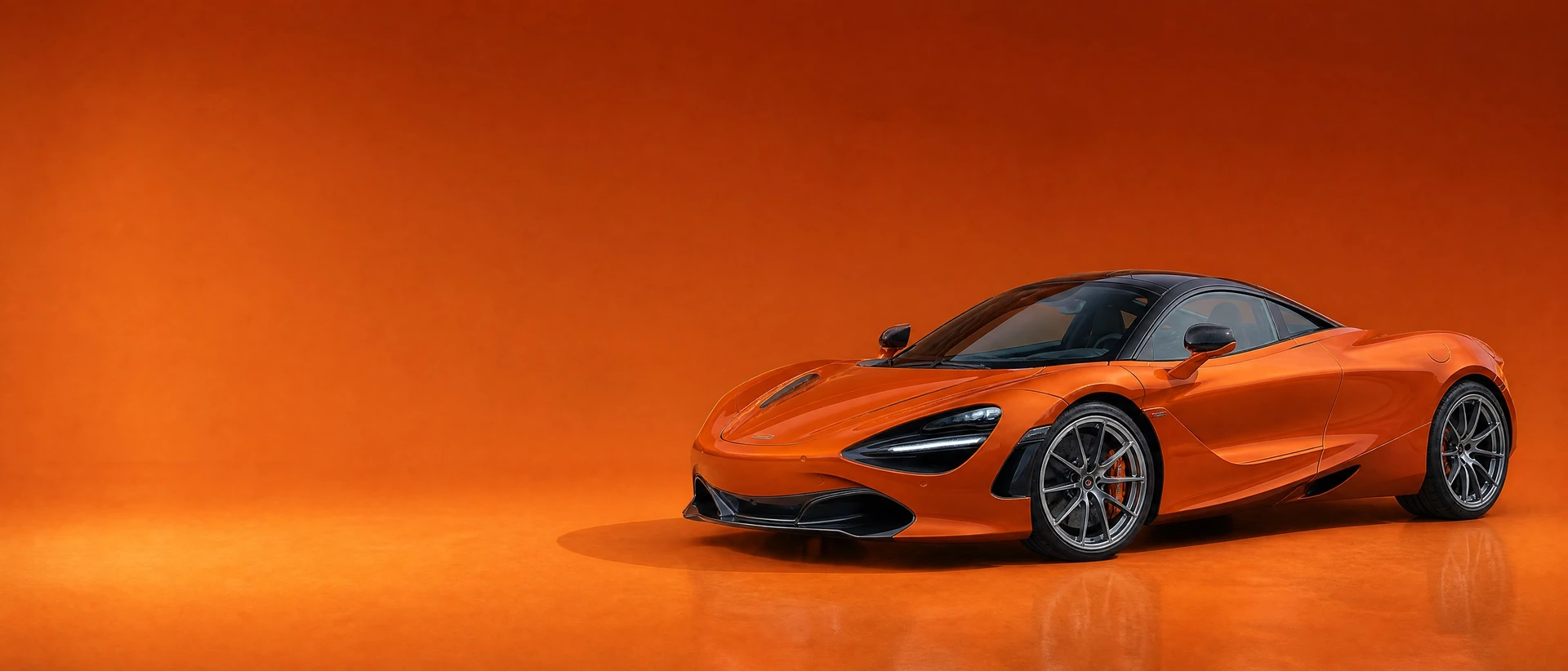 A McLaren Orange 720S, front three-quarter view on a deep burnt-orange field in warm daylight