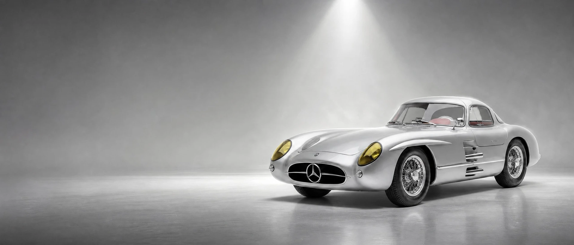 A silver Mercedes-Benz 300 SLR Uhlenhaut Coupé, front three-quarter view on a stone field with a silver beam