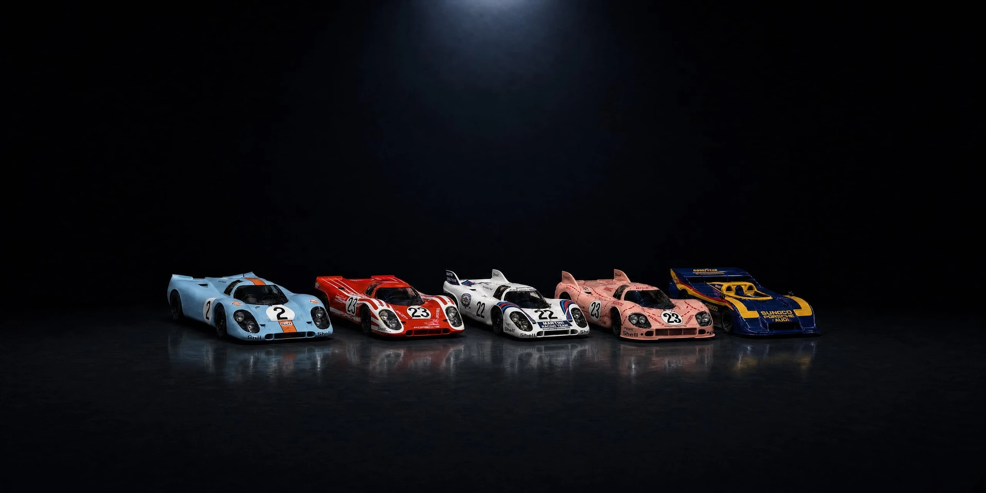 Five Porsche 917s — Gulf, Salzburg, Martini, Pink Pig and Sunoco — in one row in a near-black studio