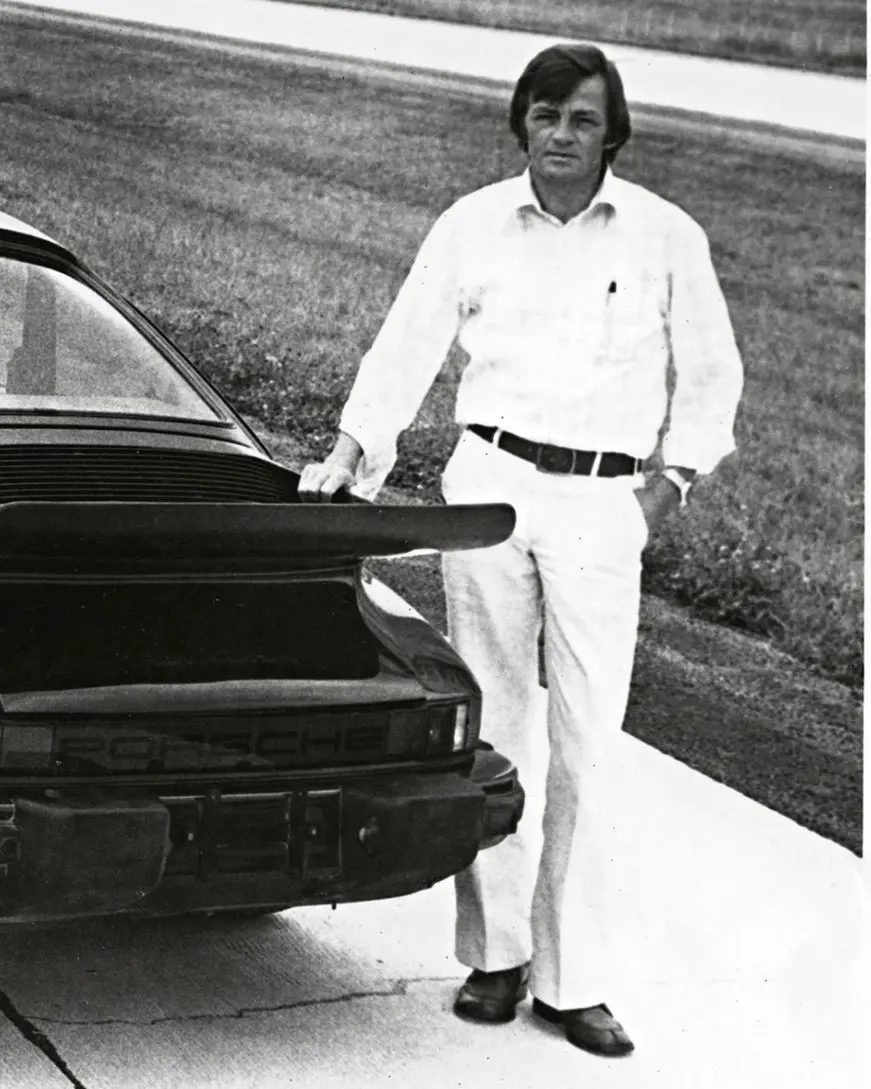 Hans Mezger in the mid-seventies, hand on the rear wing of a 911 Turbo on the test road