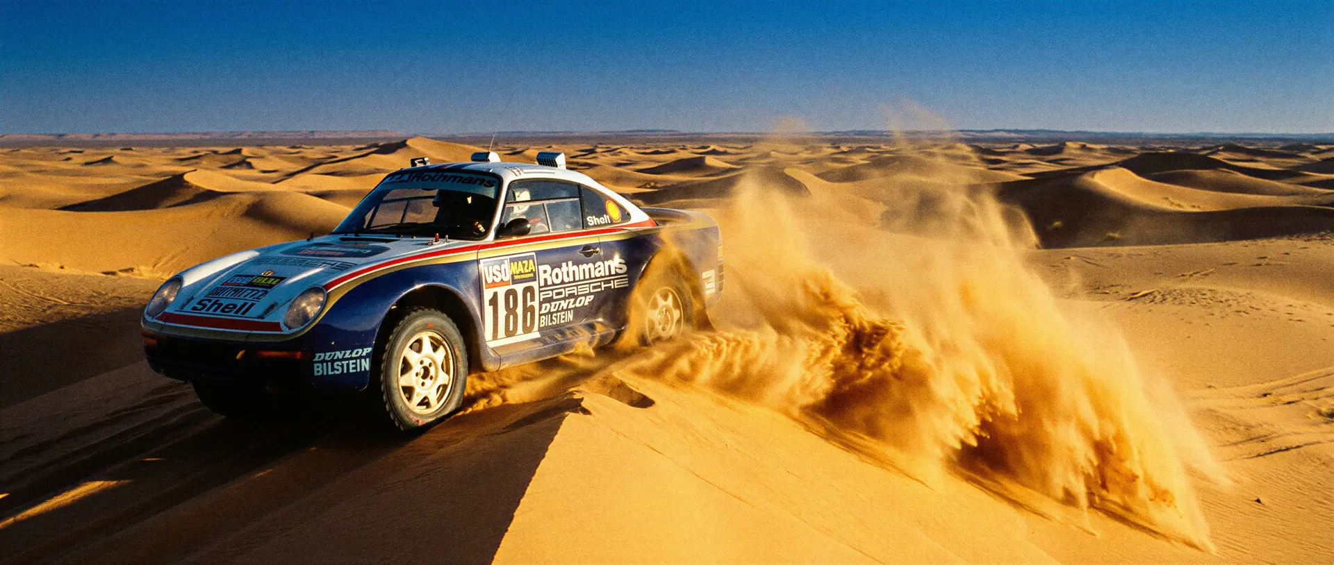 A Rothmans-liveried Porsche 959 climbing a rocky Paris-Dakar stage