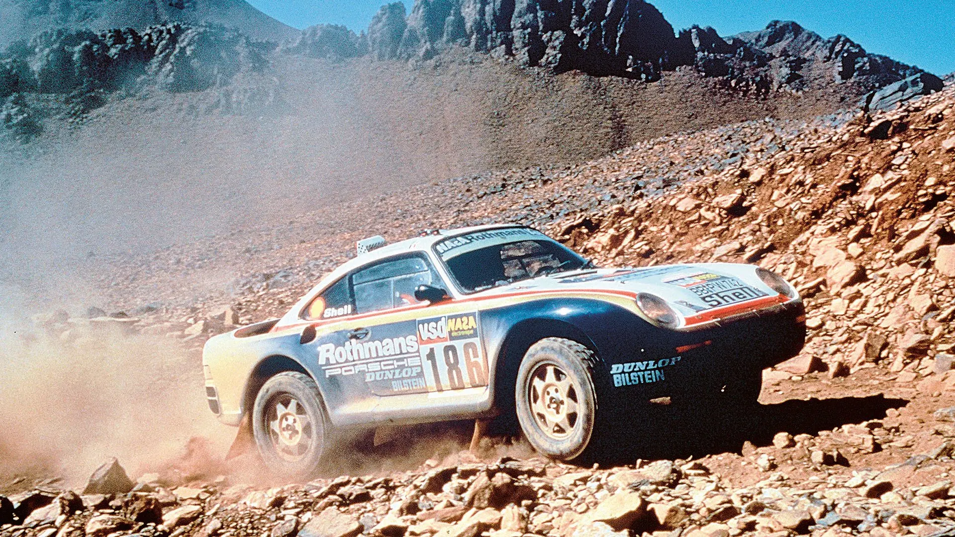 A Rothmans-liveried Porsche 959 climbing a rocky Paris-Dakar stage