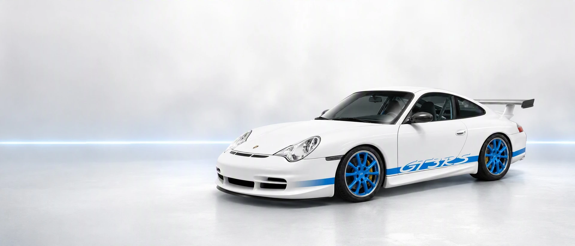 A white Porsche 996 GT3 RS with blue graphics, front three-quarter view on a misty field with a blue light line