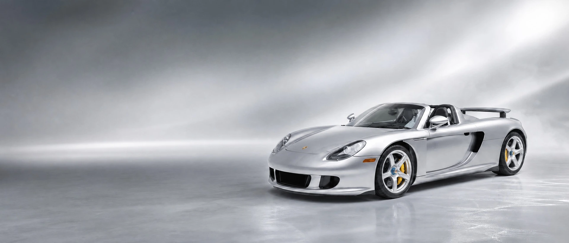A Porsche Carrera GT, front three-quarter view on a silver field with lifting mist