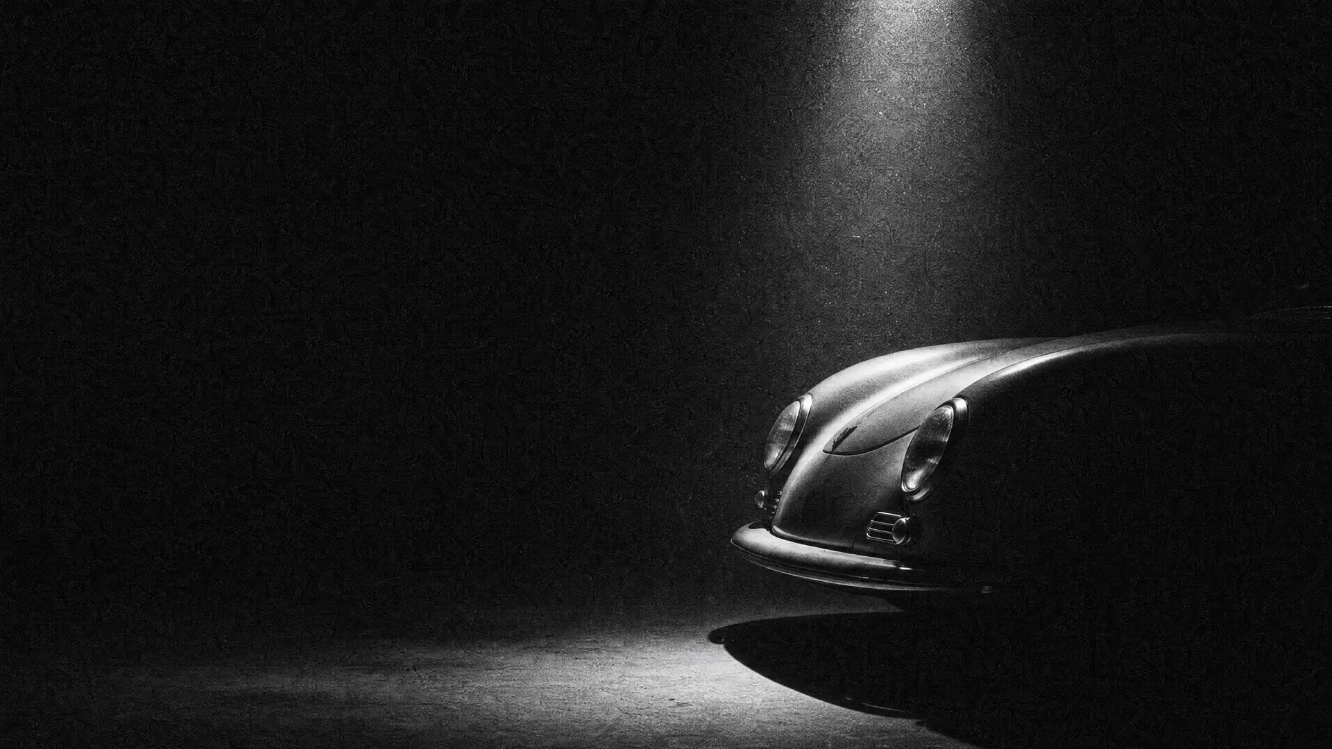 Art plate: the nose of a 1948 Porsche 356 roadster alone in a vast dark hall under one narrow shaft of light
