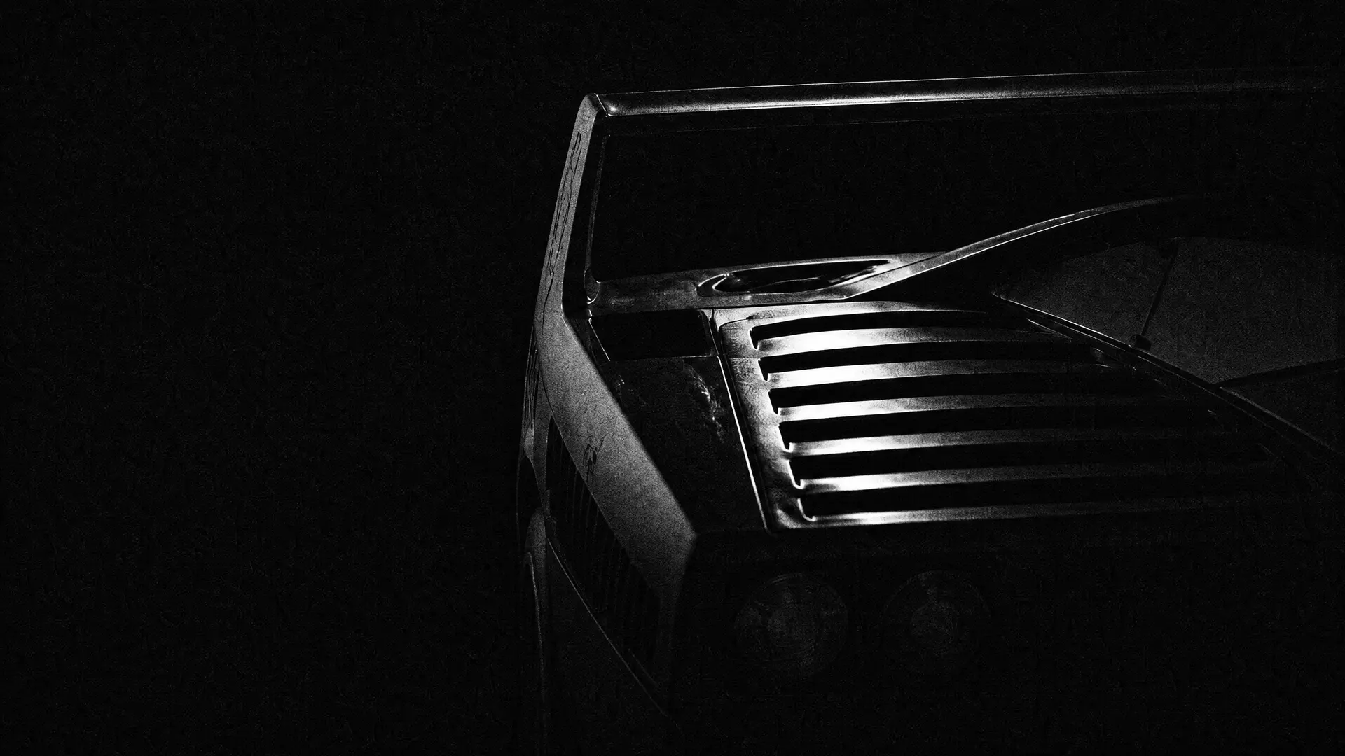 Art plate: the rear wing and louvred tail of a Ferrari F40 raked by one hard light in darkness