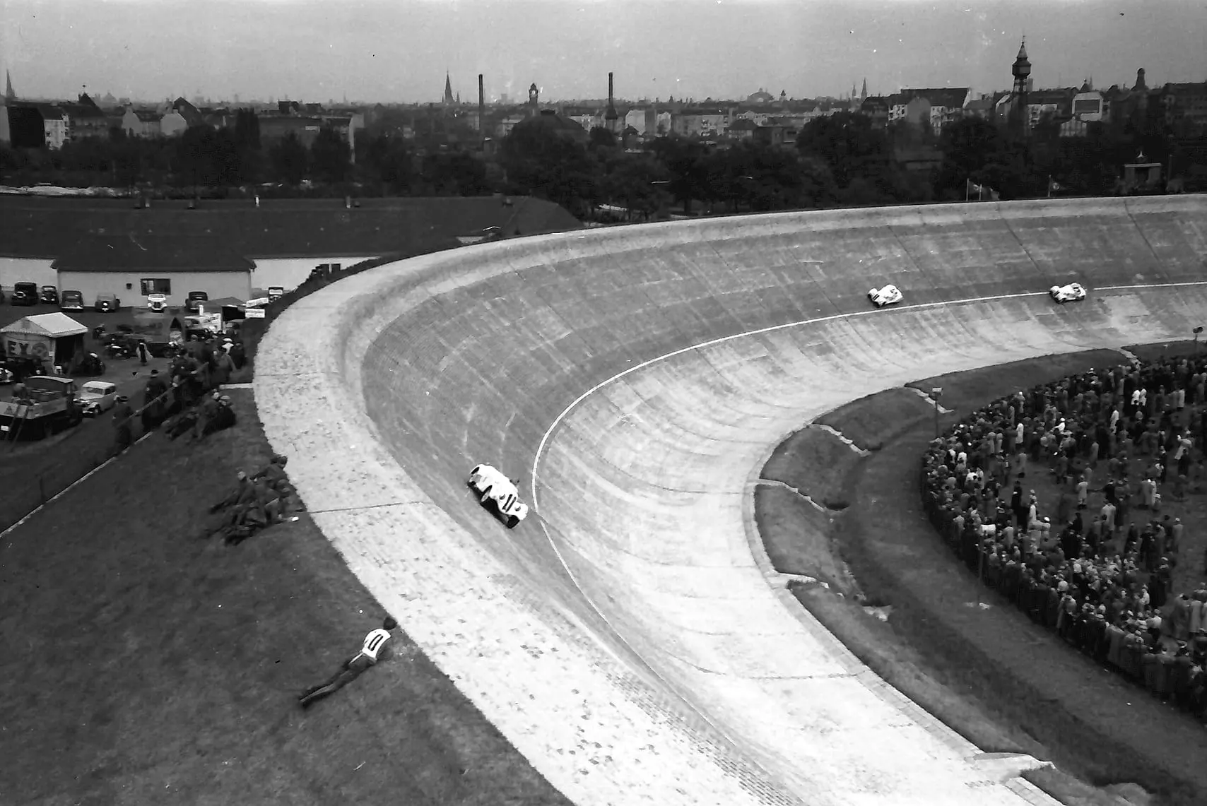 The AVUS north curve in Berlin: sports cars on the brick banking, the city behind