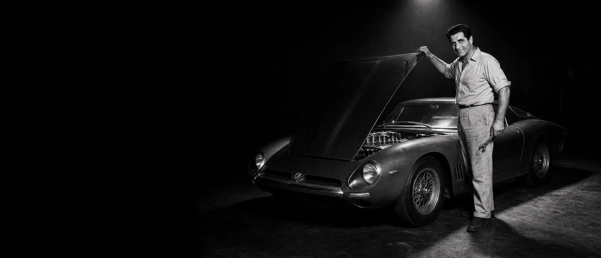 Giotto Bizzarrini leaning over the open engine bay of a Bizzarrini 5300 GT Strada under a single spotlight